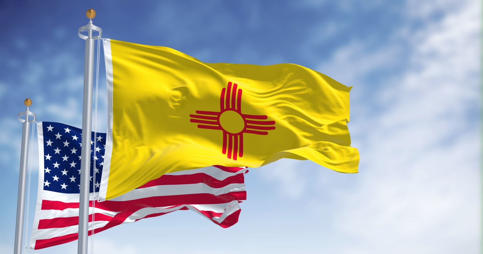 The New Mexico state flag flying with the American flag against a clear sky